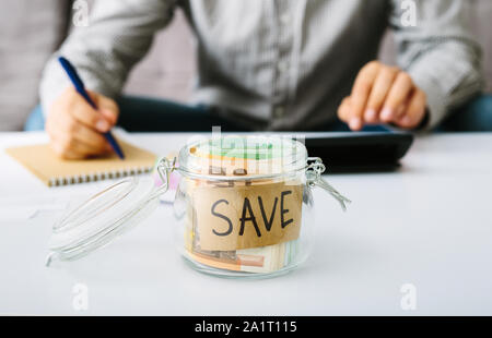 Euro bills banknote in a glass bottle for saving. Man doing his accounting. Small business: deposit and lending, interest rate reduction. Stock Photo