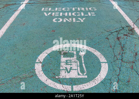 Electric Vehicle (EV) Charging Station parking spot with icon and 'Electric Vehicle Only' text on aging green painted pavement. Stock Photo