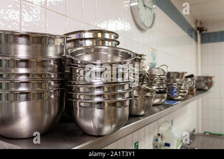 Stainless steel mixing bowls on a stainless steel shelf in an industrial kitchen Stock Photo