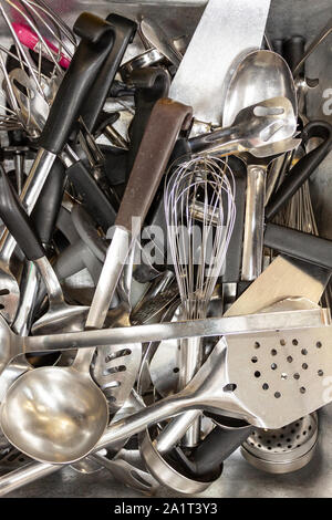 Tray of various old stainless steel kitchen cooking utensils in an industrial kitchen
