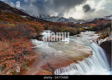 View of Mount FitzRoy with a waterfall and sunstar. The mountian is partially hidden by clouds. Stock Photo