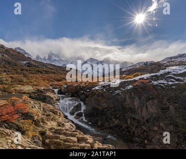 View of Mount FitzRoy with a waterfall and sunstar. The mountian is partially hidden by clouds. Stock Photo