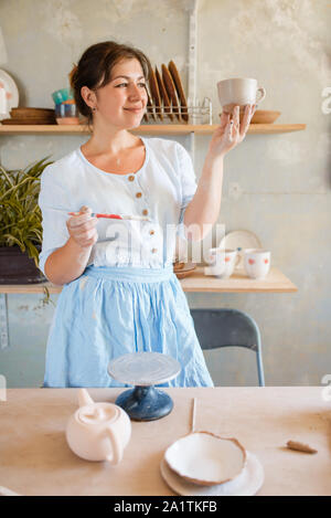 Female potter with brush paints a pot, pottery Stock Photo