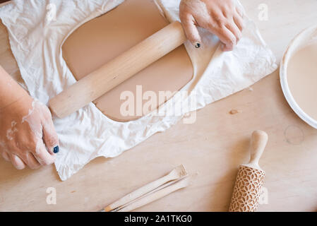 A close-up of a woman potter rolls a brown clay rolling pin on a
