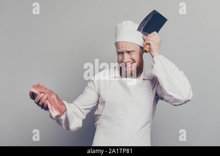 Portrait of attractive handsome butcher guy holding fresh meat and knife in arms hands touching head clueless hot to prepare cook cuisine isolated Stock Photo