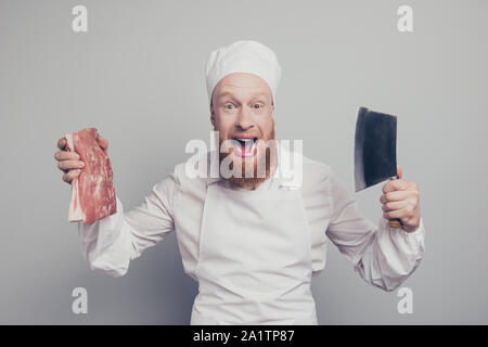 Portrait of he crazy attractive handsome cheerful cheery positive butcher guy holding fresh meat and knife in arms hands opened mouth isolated over Stock Photo