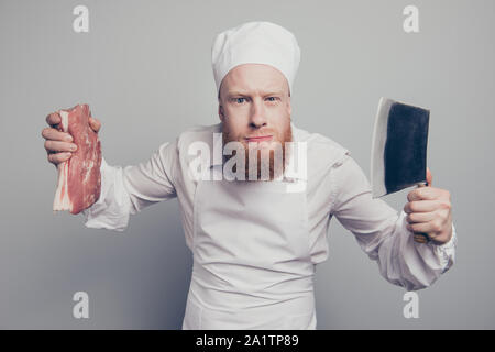 Portrait of he crazy nice attractive handsome suspicious butcher guy holding fresh meat and knife in arms hands isolated over gray pastel background Stock Photo