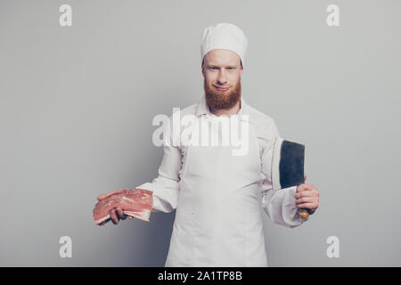 Portrait of nice calm attractive handsome butcher guy holding fresh meat and knife in arms hands prepare cook cuisine isolated over gray pastel Stock Photo