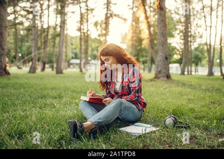 Female student writing in notebook on the grass Stock Photo