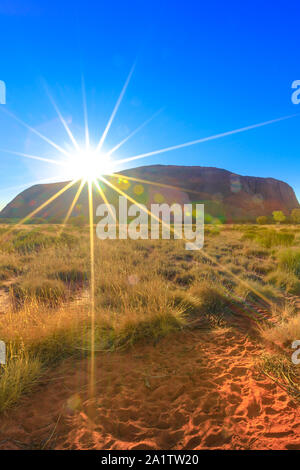 Sunbeams behind huge Ayers Rock at sunrise. Uluru illuminated by the rays of the early morning sun. Uluru-Kata Tjuta National Park, Australia Stock Photo