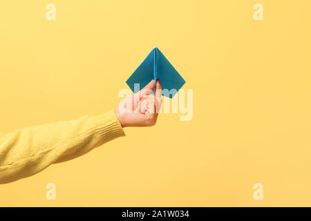 Woman hand holding blue paper airplane over yellow background, freedom concept. Stock Photo