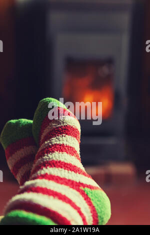 Feet legs in winter clothes wool socks at fireplace background. Woman sitting at home on winter or autumn evening relaxing and warming up. Winter and cold weather concept. Hygge Christmas eve Stock Photo