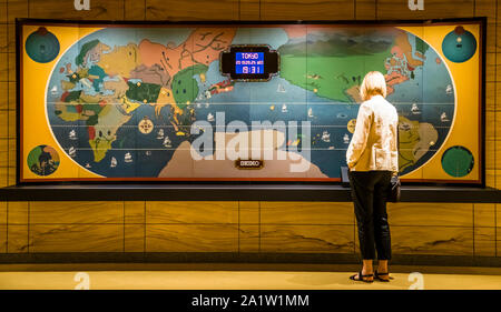 An interactive world clock from the original Hotel Okura, restored and now part of the new lobby at The Okura Tokyo, Minato ward, Japan, shows the time in individual world cities at the push of a button. A visitor reads the display for Tokyo: 7:31pm, seven hours ahead of Germany. Built by Seiko above a world map, the clock was part of the original furnishings of the hotel, which opened in 1962. Stock Photo