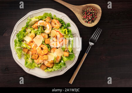 Shrimp Caesar salad with Parmesan cheese, croutons and lettuce, shot from the top on a dark rustic wooden background with copy space Stock Photo