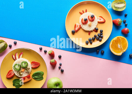 top view of plates with fancy animals made of food on blue and pink background Stock Photo