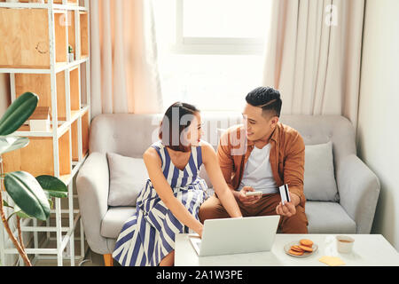 Young Asian couple paying bills by laptop and smartphone with credit card at home Stock Photo