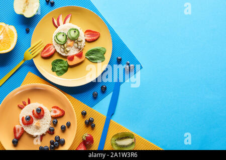 top view of plates with fancy animals made of food on blue and yellow background Stock Photo