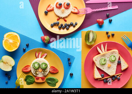 top view of plates with fancy animals made of food on blue and yellow background Stock Photo