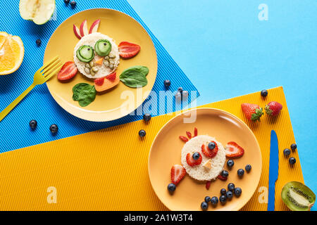 top view of plates with fancy animals made of food on blue and yellow background Stock Photo