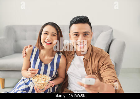 Shot of a cheeful young Asian couple watching television at home Stock Photo