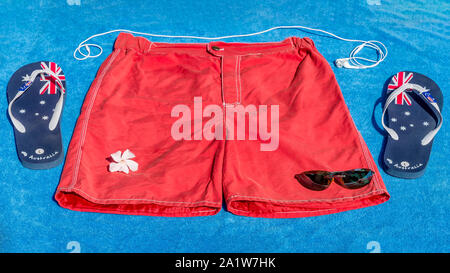 Typical male equipment for summer and the sea with swimsuit, slippers, headphones and sunglasses on a blue beach towel Stock Photo