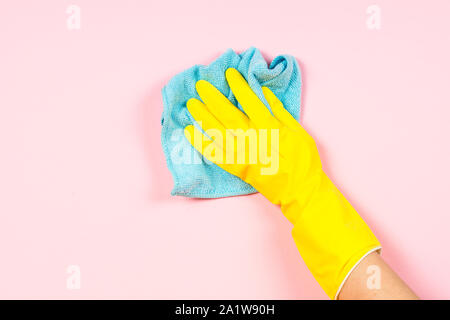Hand in yellow gloves and microfiber rag cleaning pink background. Stock Photo