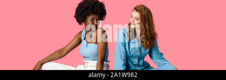 panoramic shot of cheerful multicultural women looking at each other isolated on pink Stock Photo