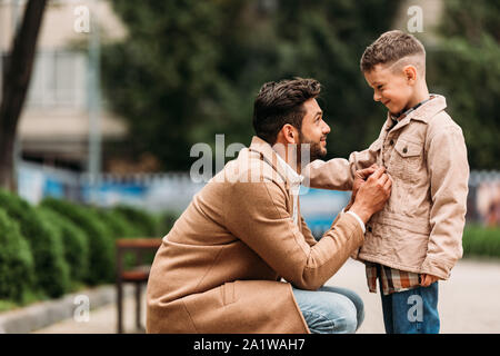 side view of dad in coat and son in jacket on street in autumn day Stock Photo