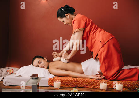 asian masseur doing back massage with herbal balls to woman in spa Stock Photo