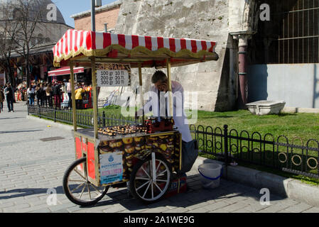Istanbul,Turkey, March 08,2019:Street vendor selling roasted chestnuts  in tradition street food cart,close up on sunny day,in front of Hagia Sophia Stock Photo