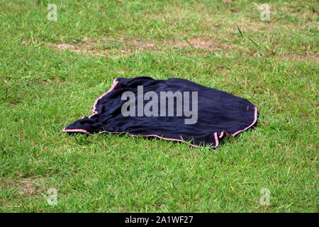 Black with red and white checkered edge picnic blanket left on uncut grass waiting for owners to enjoy and have fun on warm sunny summer day Stock Photo