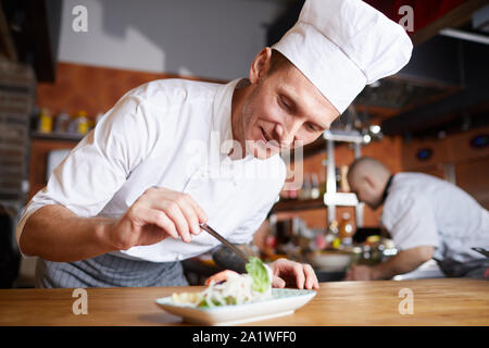 Portrait of professional chef serving elaborate Asian dish while working in restaurant kitchen, copy space Stock Photo