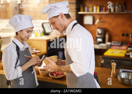 Side view portrait of professional chef training young cook taking notes while working in restaurant kitchen, copy space Stock Photo