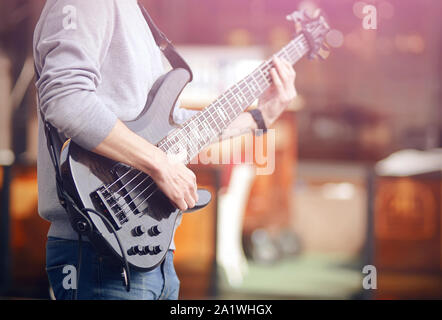 A skilled musician plays a melody at a concert on a black bass electric guitar, illuminated by light Stock Photo