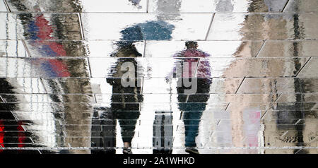 Blurry reflection silhouette on wet city street of two tourist  people walking under umbrella and  pulling traveling suitcases in the rainy autumn day