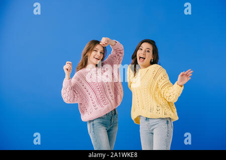 attractive and smiling women in sweaters looking at camera isolated on blue Stock Photo