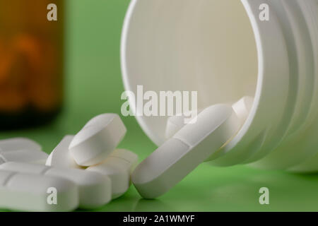 Glass and plastic medicine bottles and scattered white round tablets on a green background Stock Photo