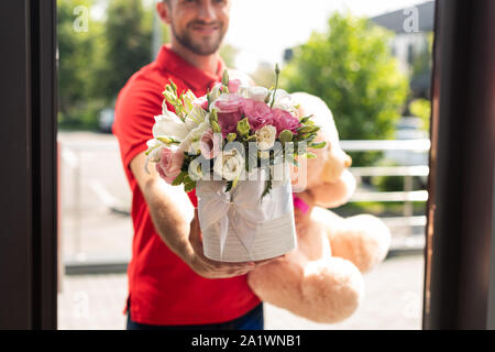 cropped view of bearded delivery man holding teddy bear and flowers Stock Photo