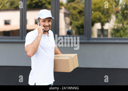 happy delivery man talking on smartphone while holding box Stock Photo