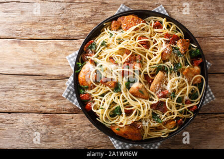 Portion of spaghetti with dried tomatoes, sliced chicken, Parmesan and spinach, close-up on a plate on the table. Horizontal top view from above Stock Photo
