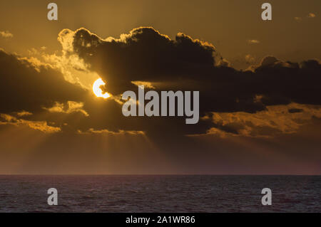 Setting sun hides behind the clouds over a dark purple Caribbean Sea. Stunning Cloudscape. Stock Photo
