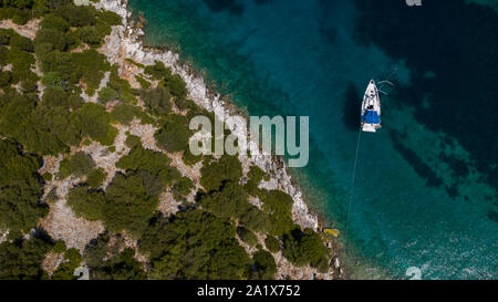 Aerial photo of a sailing yacht at anchor in a sheltered Greek coastline in the clear blue Summer Mediterranean sea