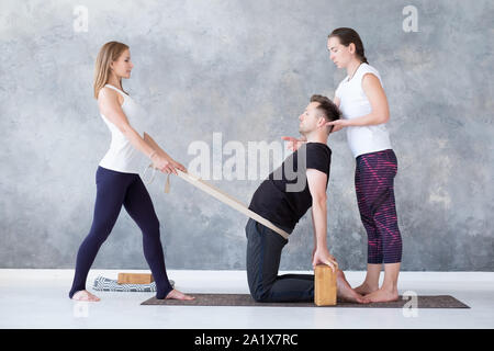 Man doing camel yoga pose in gym with his instructors help. Stock Photo