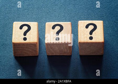 Row of three question marks on wooden blocks viewed high angle centered on a textured blue background Stock Photo