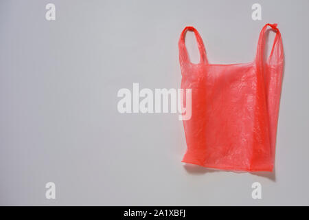 Crumpled red plastic single use carrier bag or shopping bag on grey with copy space in a conceptual image Stock Photo