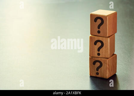 Stack of three wooden cubes with question marks forming a side border over a graduated grey background with copy space Stock Photo