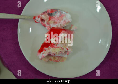 A beautiful piece of strawberry cake and cream serve on white plate isolated on purple table cloth. Stock Photo