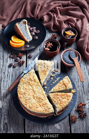 delicious Poppy Seed Crumble Cheesecake sliced on a black stone plate with cups of coffee, knife and brown cloth on a rustic wooden table, vertical vi Stock Photo