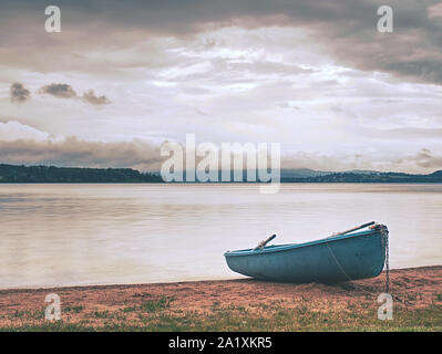 Lonely fishing vessel boat docked on beach at calm lake. Laminate or wooden fishing boat in a still lake water Stock Photo