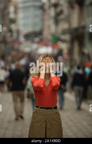 Panic attack in public place. Woman covers his eyes with hands at standing in the middle of a busy street. Stock Photo